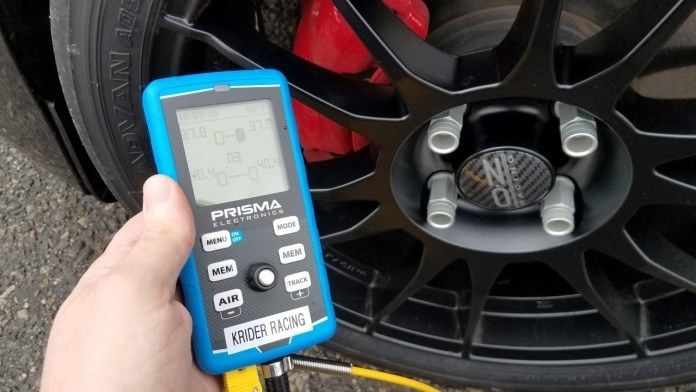 Handheld tire pressure gauge beside a black performance wheel and red brake caliper