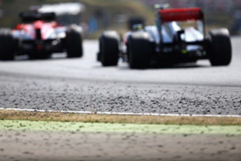 Two open-wheel race cars driving over a visibly textured circuit surface